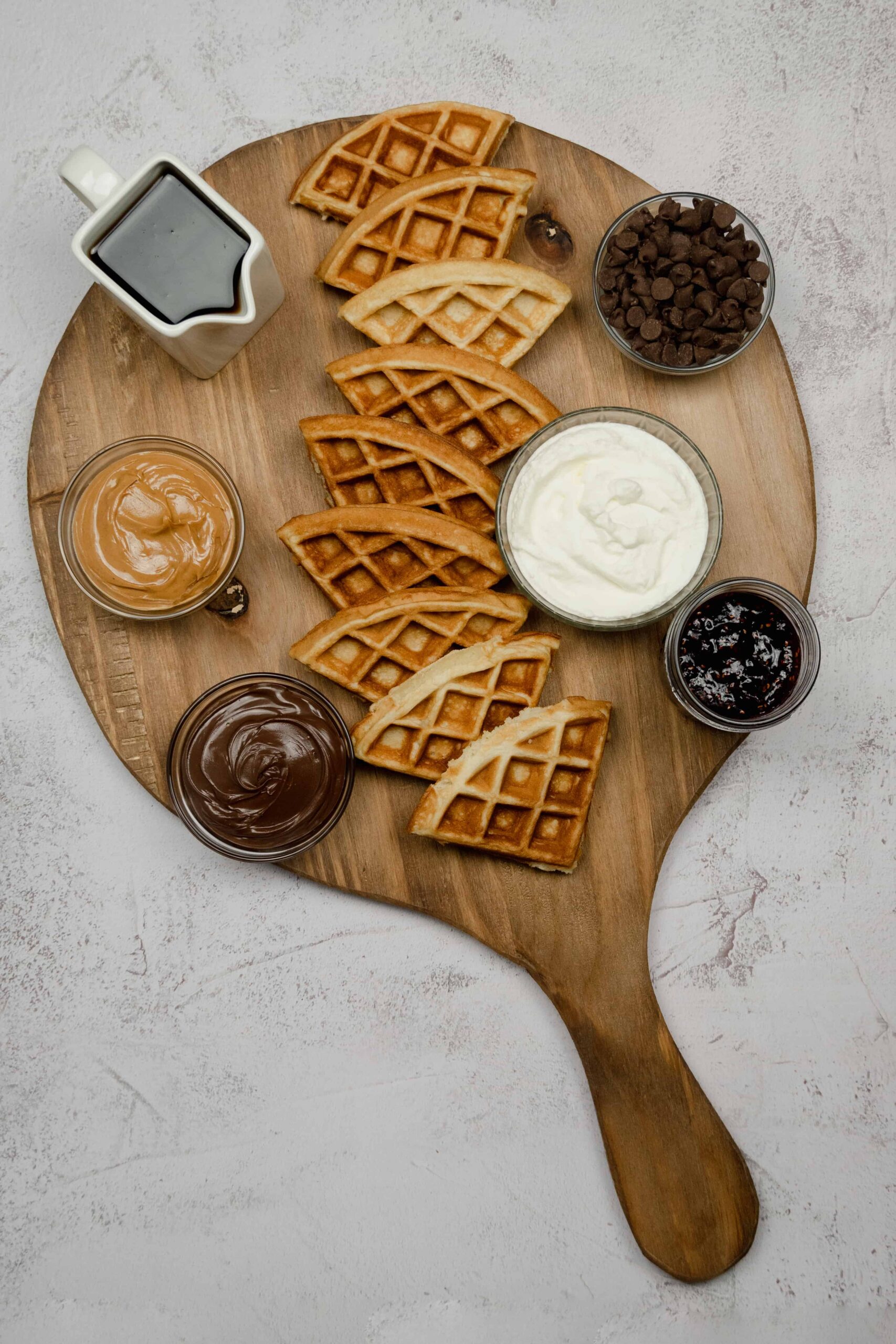 Waffles and bowls of toppings on a wooden charcuterie board.