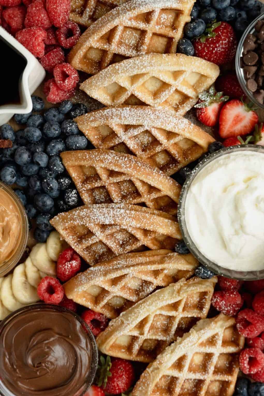 Breakfast charcuterie board up close with waffles and fruit topped with powdered sugar.