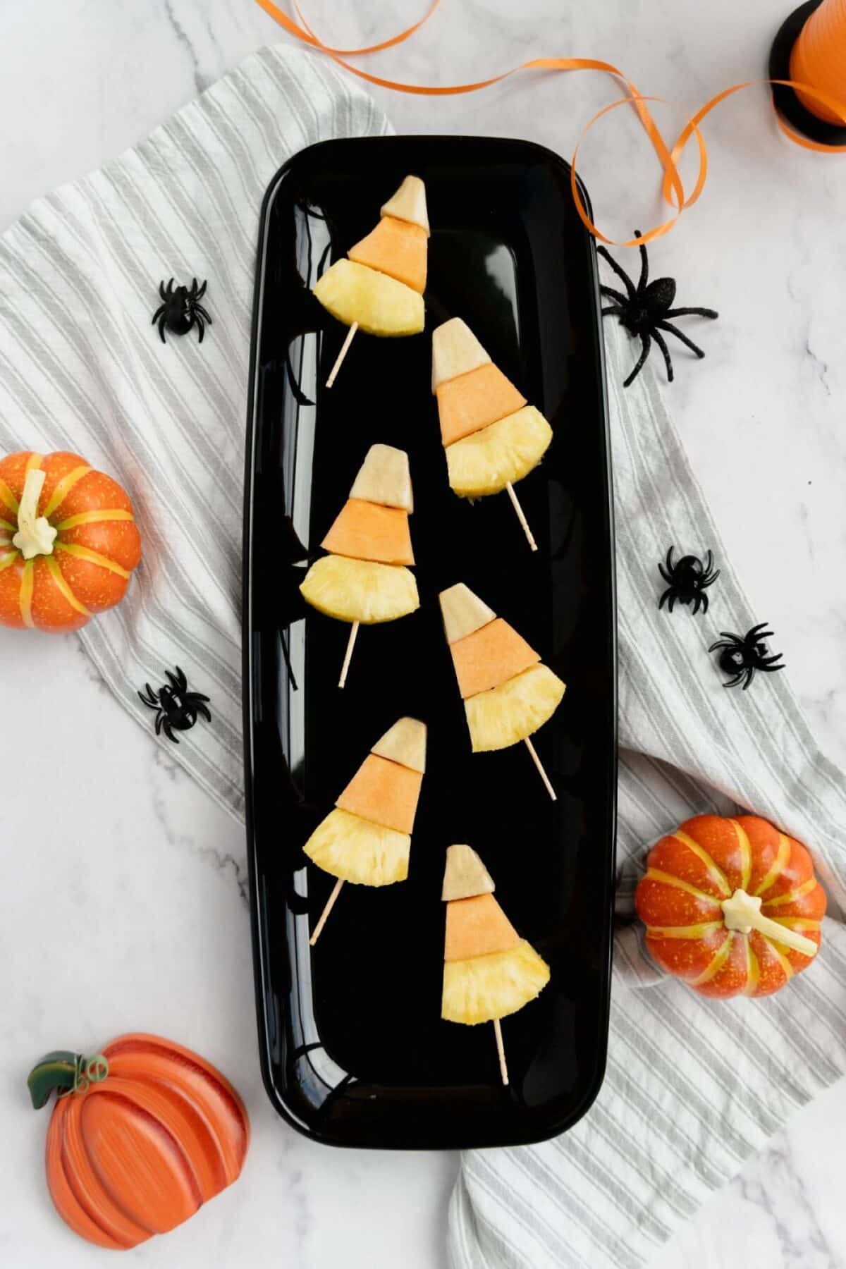 Candy corn fruit kabobs healthy halloween snack on a black plate.