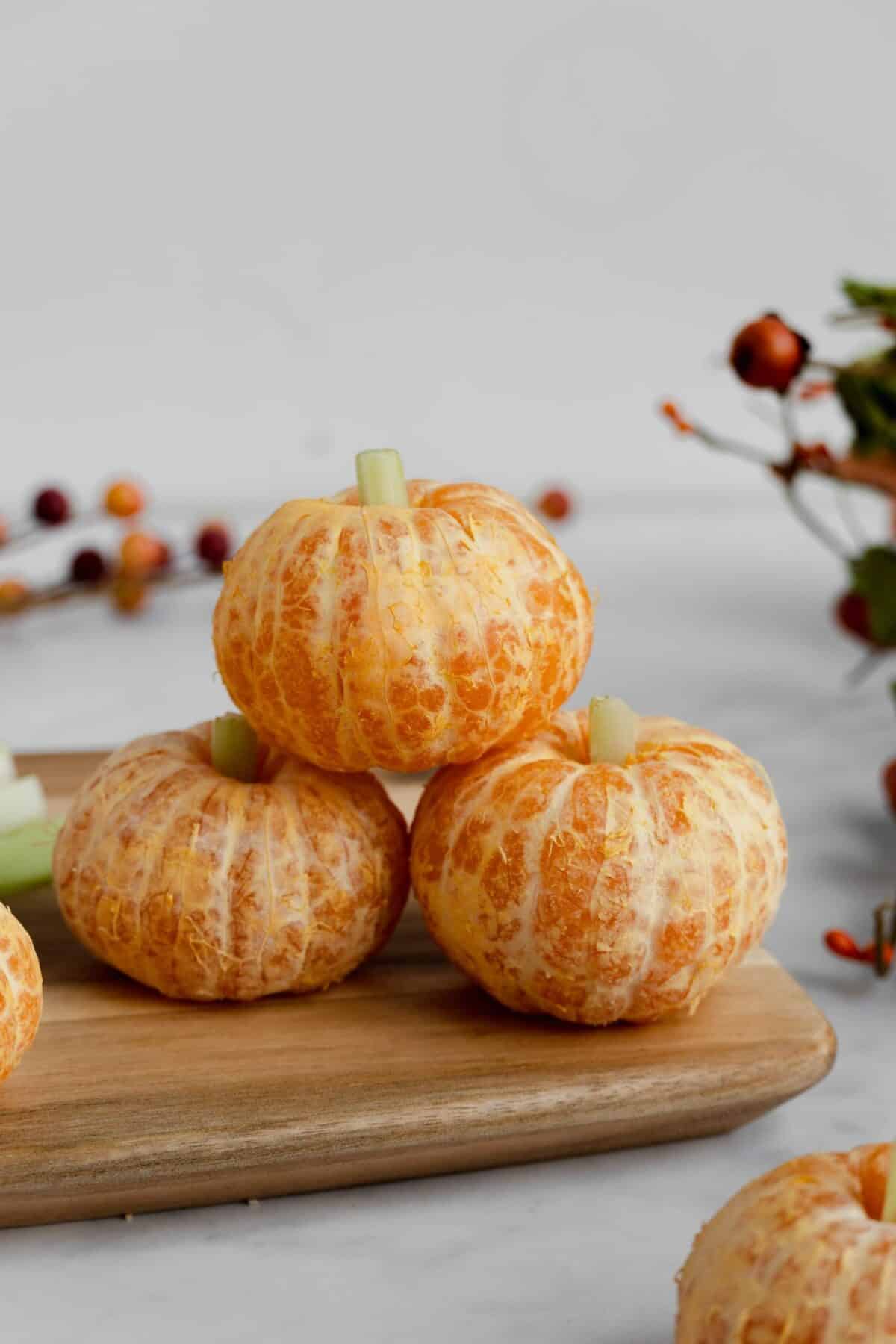Healthy halloween snack of clementine pumpkins with celery stems stacked on a wooden cutting board.