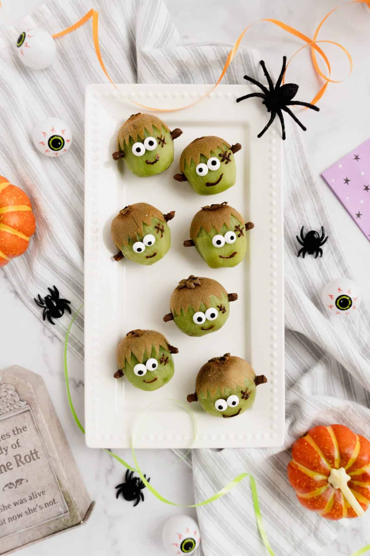 Healthy halloween Frankenstein kiwis on a white platter.